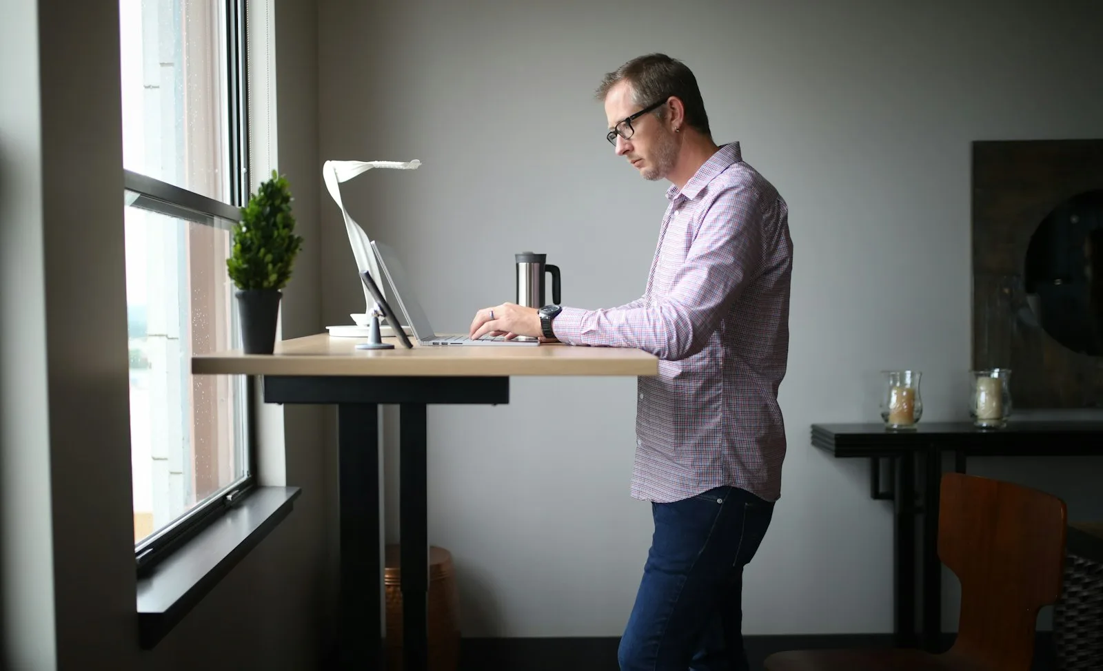 Man standing at a wooden standing desk in an office, wearing regular dress shoes rather than an anti-fatigue mat setup
