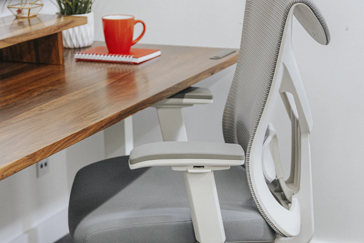 Ergonomic office chair with adjustable armrests and mesh back sitting at a wooden desk