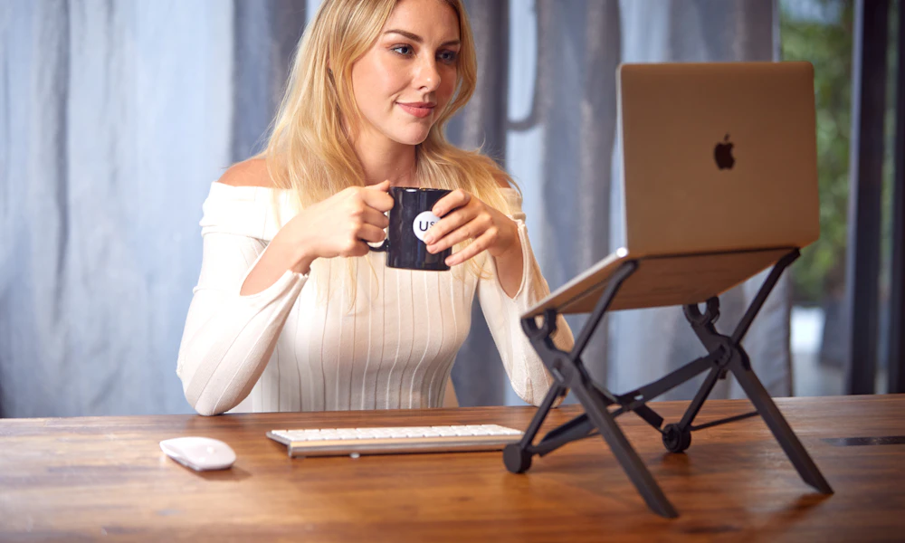 Woman working on a laptop at a cafe table with a portable laptop stand, a typical use case for a foldable stand