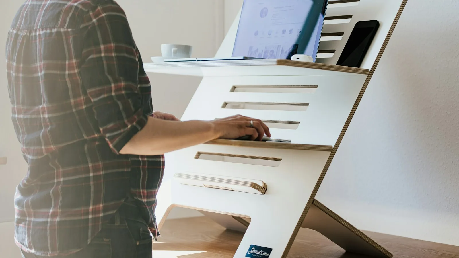 Person standing at a desk using a laptop on a raised platform in a home office