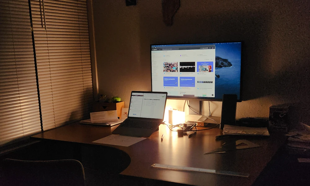 Open laptop next to an external monitor on a desk, a dual-screen setup where a horizontal stand keeps both screens usable