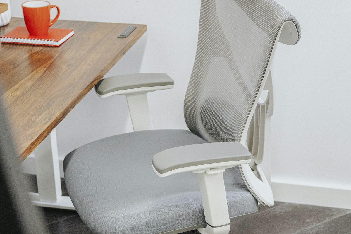 Lumbar Cushion for Car vs Office Chair: What's the Difference? 2 A gray office chair with a lumbar cushion strapped to the backrest, positioned at a wooden desk