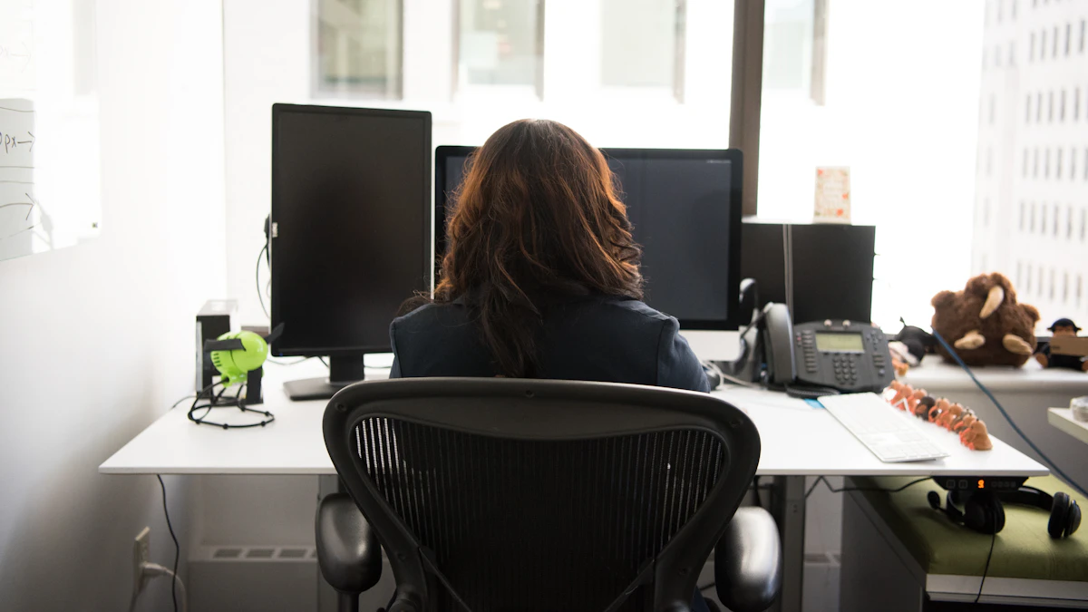 How to Sit Properly in an Office Chair for Back Pain 1 Person sitting at a desk in an office chair, working at a computer with a posture that shows a typical seated home office setup