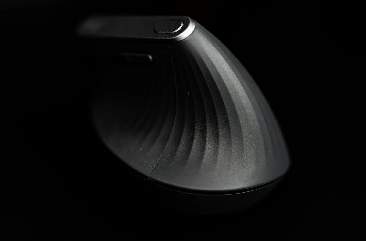 Curved gray ergonomic mouse with a contoured shape designed to fit the hand, shown against a dark background