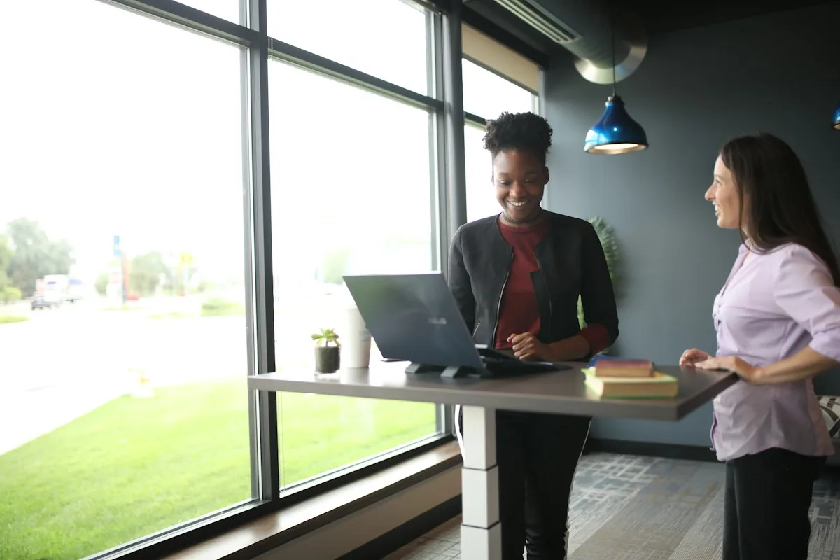 Signs Your Standing Desk Motor Is Failing 2 Two people standing at a height-adjustable desk with a laptop, one side of the desk column visible