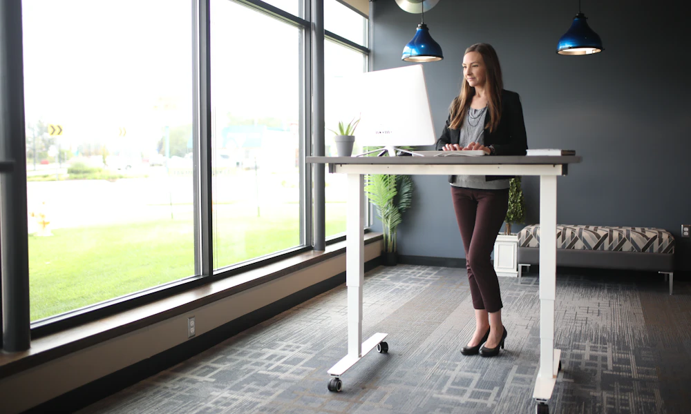 Woman standing at an adjustable standing desk in front of a window